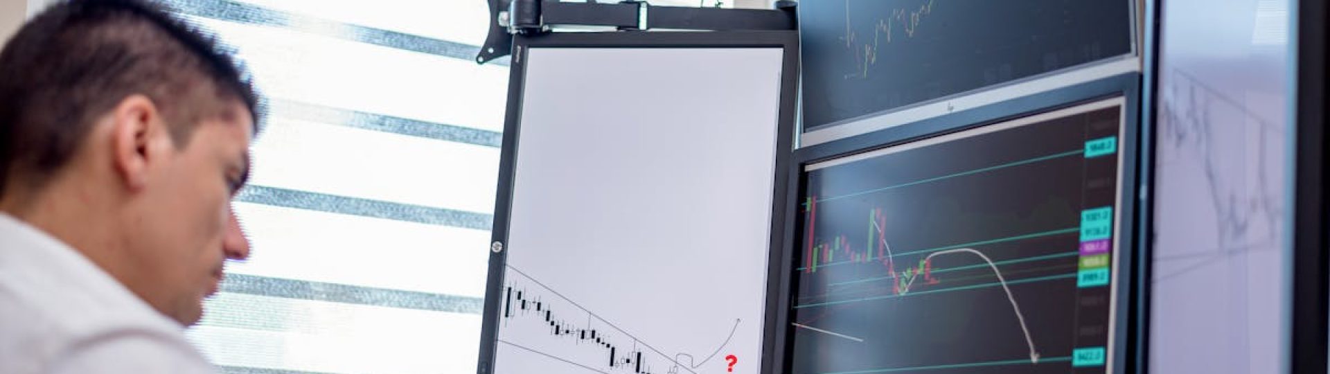 A stock trader analyzes financial data on multiple computer screens in an office setting.