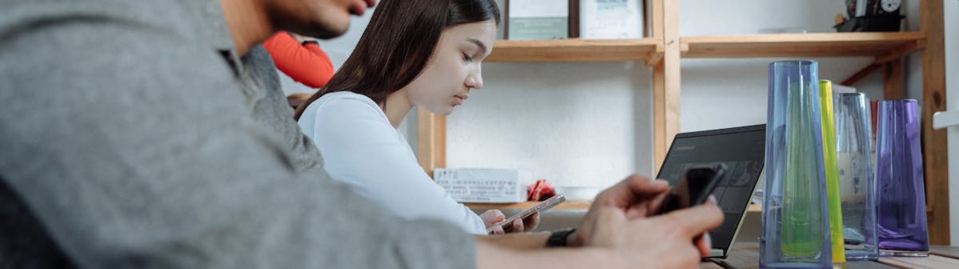 Students focused on smartphones and laptops in a modern classroom setting.