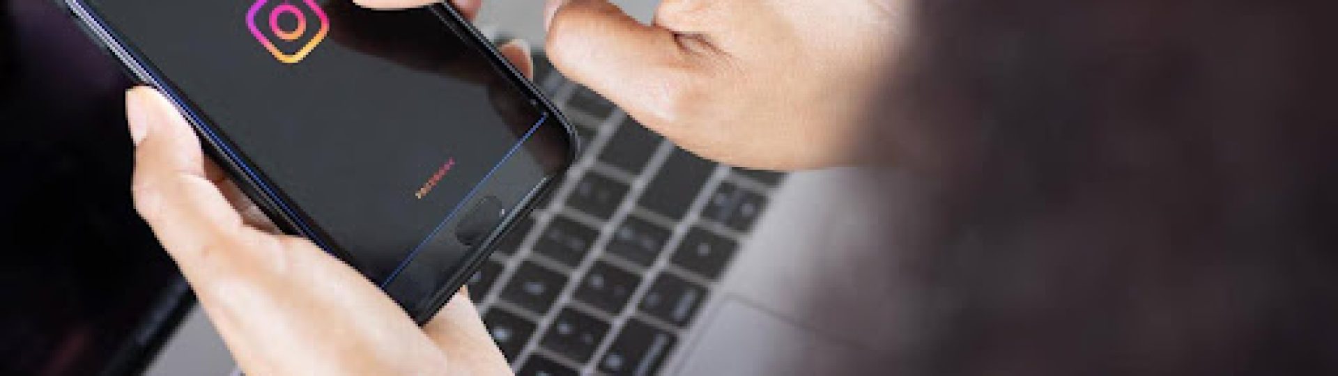 Person holding a smartphone with the Instagram logo on screen above a laptop keyboard