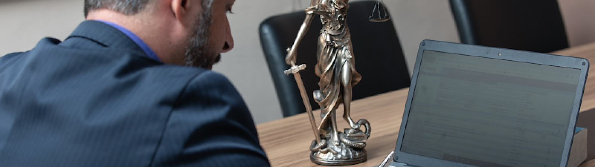 Lawyer writing beside a laptop and Lady Justice statue in a conference room
